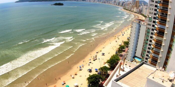 Aerial view of a crowded beach with high-rise hotels along the coast and a small island in the distance.
