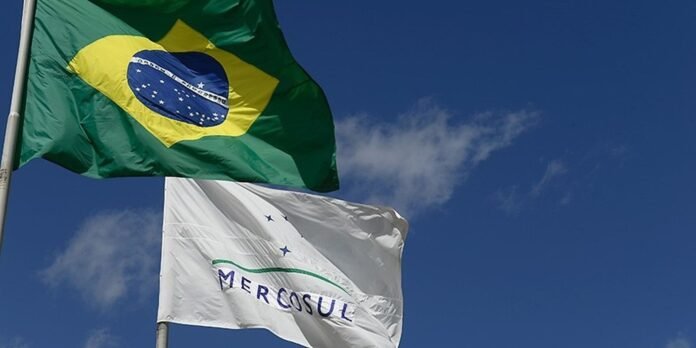 Brazil flag and Mercosul flag fluttering in a clear blue sky.