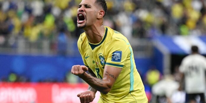 Brazilian soccer player in a yellow jersey celebrating a goal with clenched fists and mouth open.