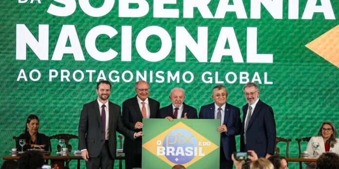 Six people in suits pose on a stage holding a green sign that reads 'PIX É DO BRASIL' with a large green backdrop displaying white text.