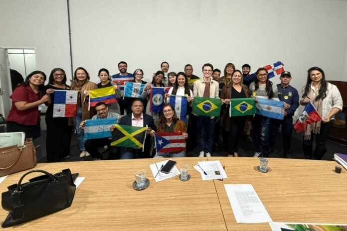Group of diverse adults in a meeting room posing for a photo while holding multiple national flags (Brazil, Argentina, Jamaica, Panama, Puerto Rico, etc.). It looks like an international or cultural event.