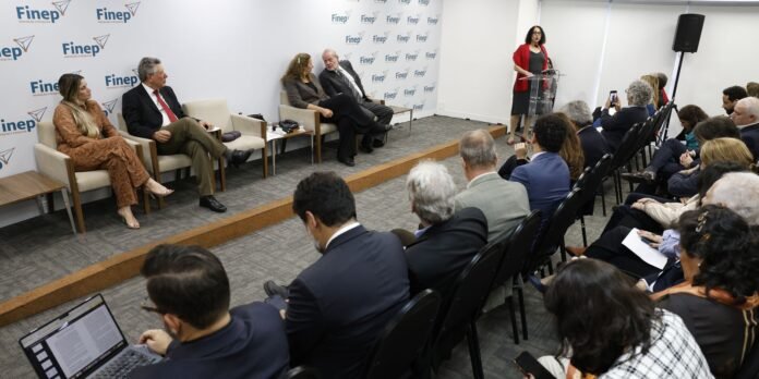 Panelists seated on stage during a conference, with a speaker at the podium addressing the audience. Backdrop shows Finep branding.