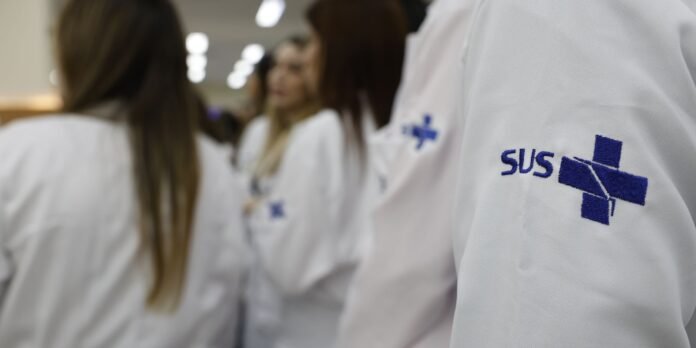 Healthcare professionals in white coats with SUS logo in a blurred hospital hallway.
