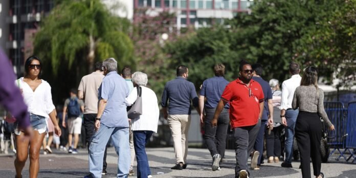 Diverse group of people walking away on a sunny urban street, trees and buildings in the background, casual attire. Taken from behind the crowd.