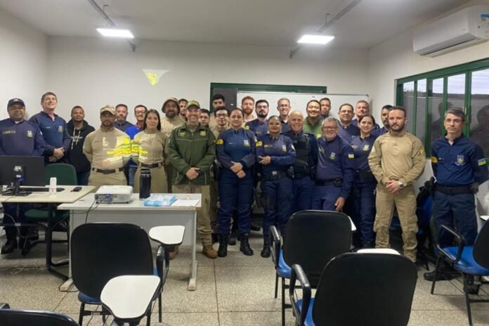Group of uniformed professionals posing together in a training room with desks and a whiteboard behind them.
