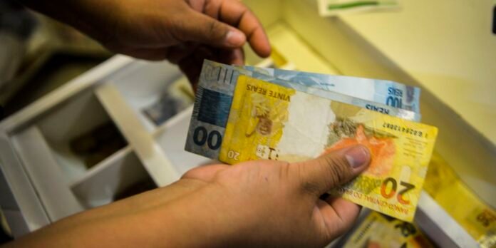 Hands counting Australian banknotes (20 and 100 dollar bills) at a cash register drawer.