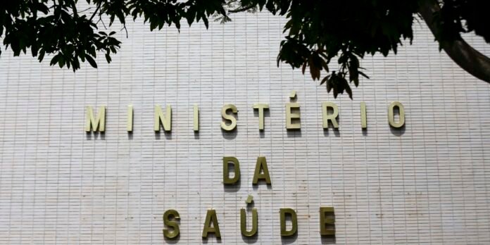 Exterior wall with gold letters forming 'MINISTÉRIO DA SAÚDE' on a light tiled surface, with tree branches overhead.