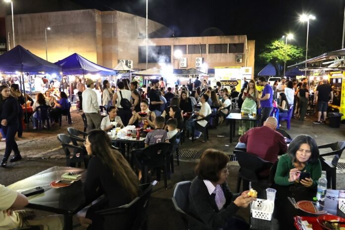 Night market scene at night with blue tents, food stalls, and people dining at outdoor tables.