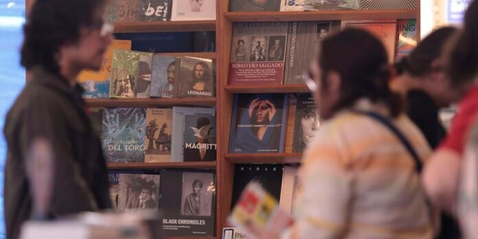 Blurred bookstore scene with wooden shelves filled with magazine and book covers; several people stand and browse in the foreground.