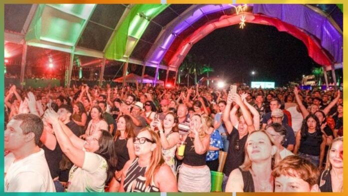 Large outdoor concert crowd under colorful canopy, people raising hands and enjoying the performance at night.