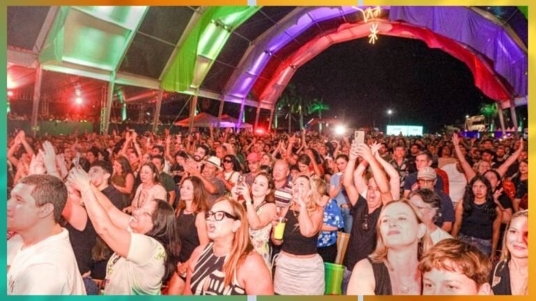 Large outdoor concert crowd under colorful canopy, people raising hands and enjoying the performance at night.