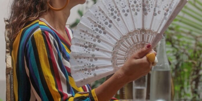 Person in a bright striped shirt holding a white lace hand fan outdoors.