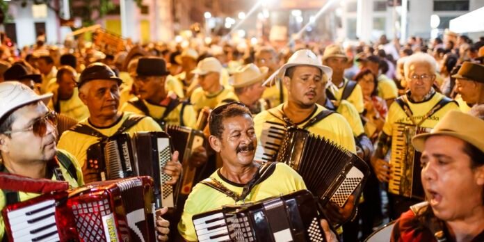 Group of street musicians wearing yellow shirts playing accordions at a crowded nighttime parade or festival.