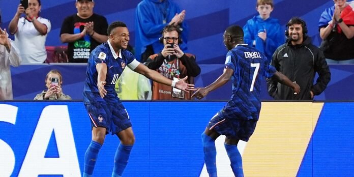 Two soccer players in blue uniforms celebrate a goal, reaching out to high-five with cheering fans in the background.