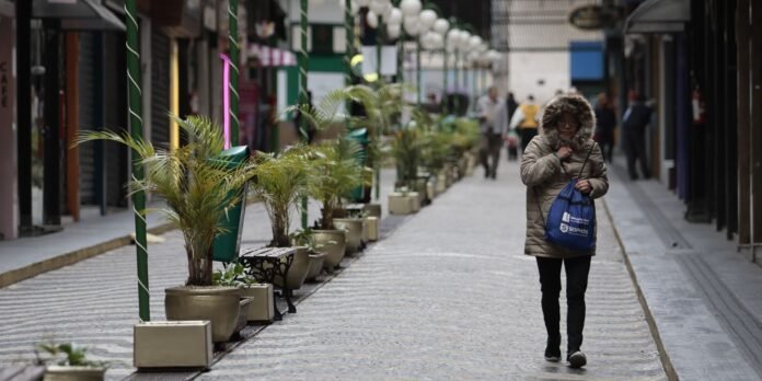 Woman in a beige hooded coat walks down a cobblestone street carrying a blue bag.
