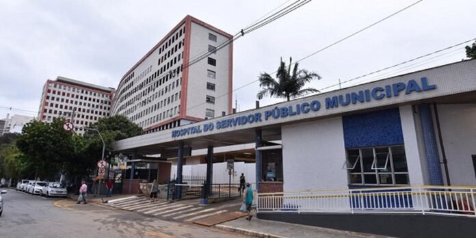 Front view of Hospital do Servidor Público Municipal with blue signage, entrance canopy, and pedestrians crossing the street near a crosswalk.