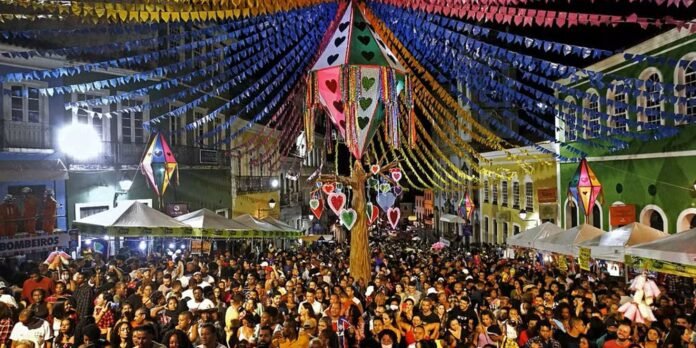 Crowded night festival on a city street with vibrant bunting, heart-shaped lanterns, and market stalls.