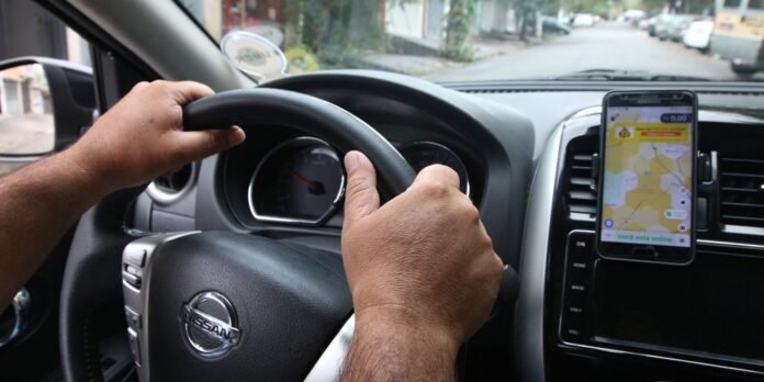 Driver's hands on the steering wheel of a Nissan, with a navigation map visible on a phone mounted to the dashboard.