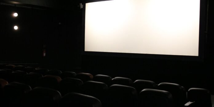 Dimly lit movie theater with a large blank projection screen and rows of empty seats facing it
