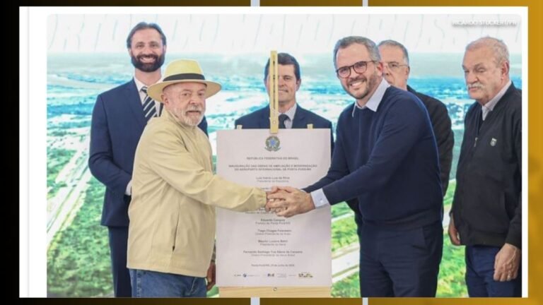 Grupo de homens em traje formal e casual, apertando as mãos diante de um grande certificado em uma cerimônia.