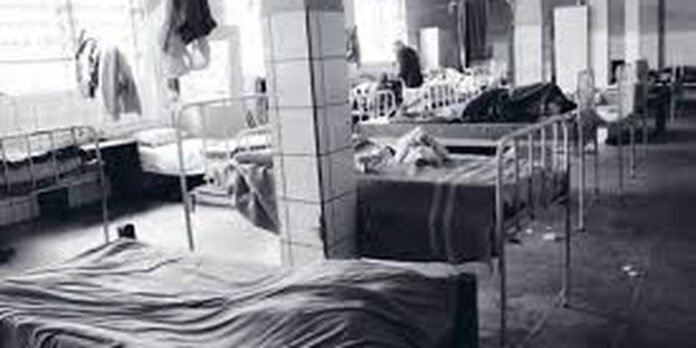 Grayscale hospital ward with multiple beds and curtains along each side.