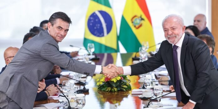 Two men in suits shake hands across a conference table with Brazil and Moldova flags in the background, during a formal meeting.