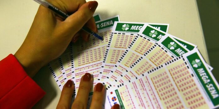 Close-up of a hand with red nail polish filling out a MEGA-SENA lottery ticket spread on a table.