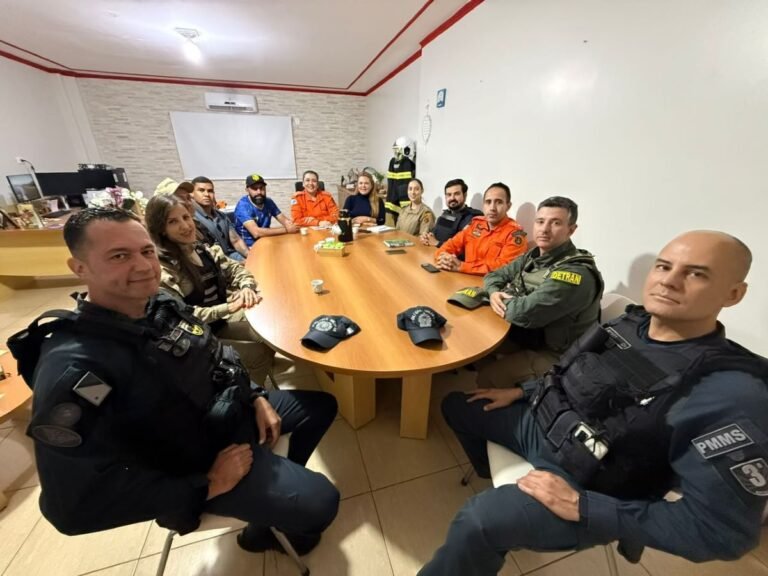 Group of uniformed officers and civilians seated around a wooden conference table in a briefing room.