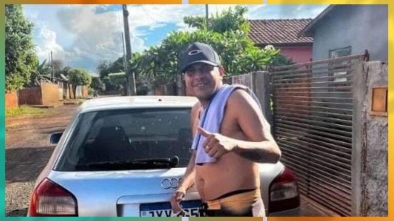 Shirtless man with a towel over his shoulder stands beside a silver car on a suburban street, pointing at the camera.