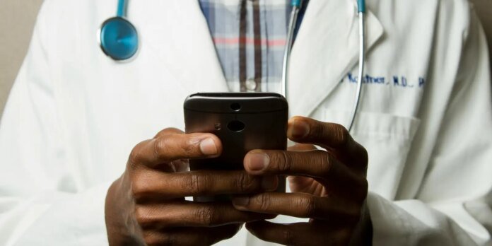 Doctor in a white coat with a stethoscope around the neck uses a smartphone.