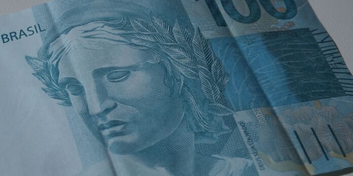 Close-up of overlapping blue Brazilian 100 real notes, showing a sculpted head with a laurel wreath and intricate patterns.