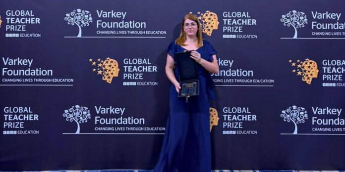 Woman in a blue gown holding an award on a red carpet in front of a Global Teacher Prize backdrop.