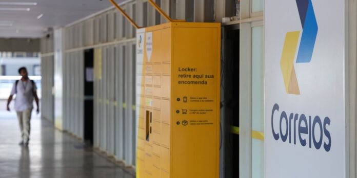 Yellow parcel locker unit in a corridor beside a large Correios sign; a blurred person walks in the background.
