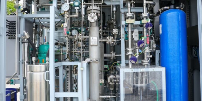Complex industrial control cabinet with stainless steel pipes, gauges, valves, and a blue pressure tank on the right; appears to be part of a processing or gas/liquids system.