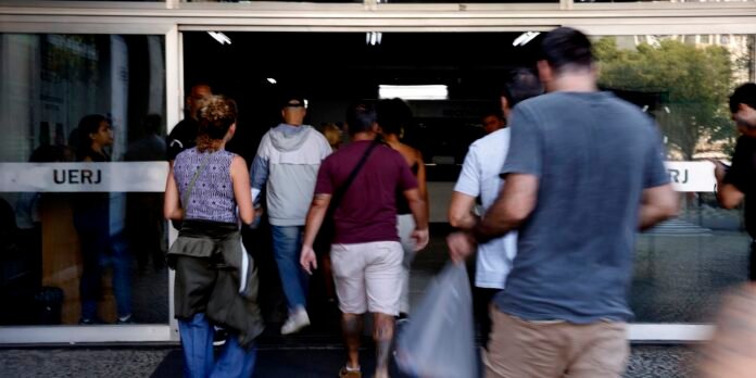 Crowd of people entering a building through glass doors labeled UERJ.