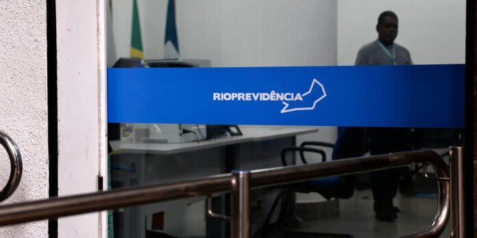 Blue Rio Previdência sign across a glass door with an office interior and a person standing in the background.