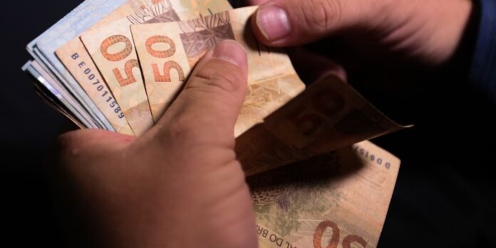 Hands count a fan of €50 euro banknotes in a dark background.