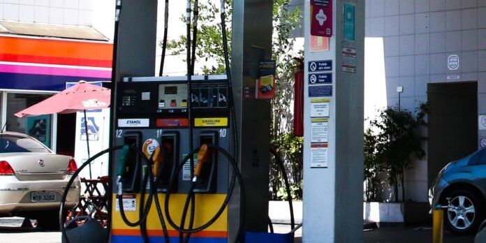 Gas station with multiple fuel pumps and coiled hoses, a car parked nearby in the background at left.