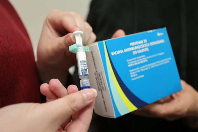 Close-up of hands preparing a syringe and vial beside a vaccine box, ready for an injection