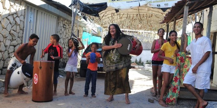 Group of kids and a woman playing drums in a sunny alley, making music together