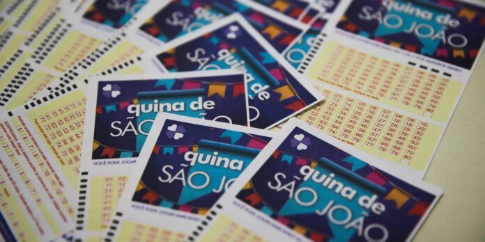 Colorful lottery cards scattered on a table, reading 'quina de São João' with a blue clipboard graphic.