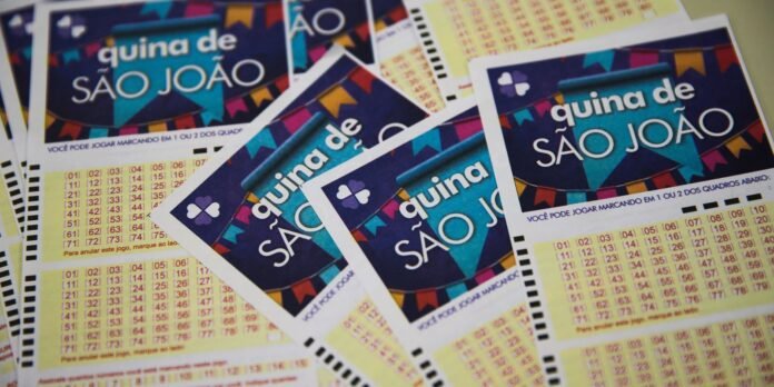Colorful lottery cards titled 'quina de SÃO JOÃO' arranged in a pile, showing bold text, festive borders, and number grids on yellow sections.