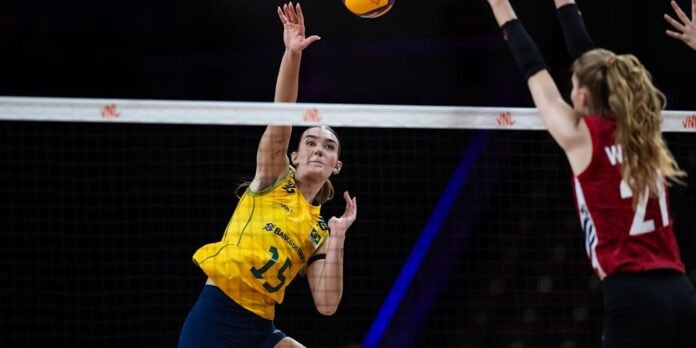 Brazilian volleyball player in yellow (#13) leaps to spike the ball over the net as a defender in red (#21) jumps to block from the opposite side.