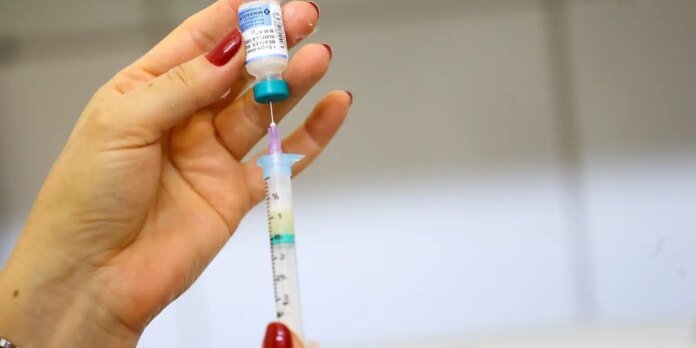 Close-up of a hand drawing liquid from a labeled vial into a syringe, preparing an injection.