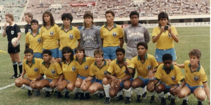 Brazilian youth soccer team posing for a group photo on a grassy stadium field, wearing yellow shirts and blue shorts with a gray goalkeeper jersey in back row.