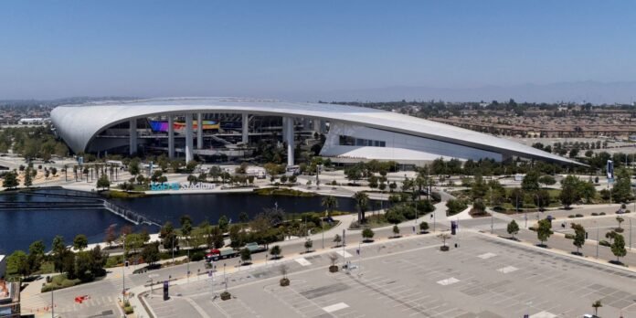 Aerial view of SoFi Stadium with its curved white roof, a reflecting pond, and landscaped foreground