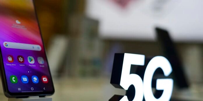 Smartphone with a colorful home screen next to a large illuminated 5G sign.