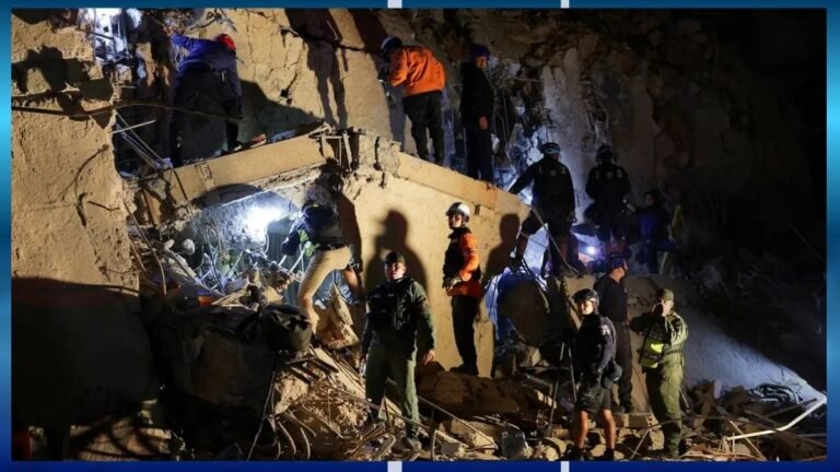 Emergency responders on rubble during a nighttime rescue operation at a collapsed building site.