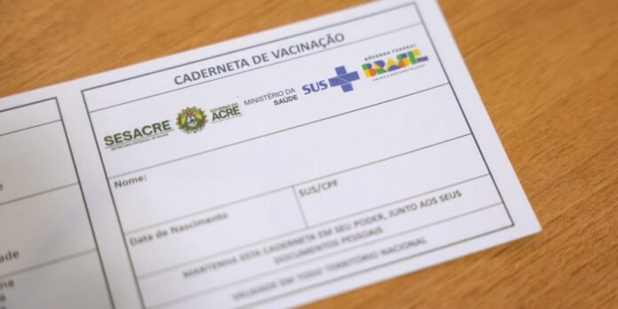 Vaccination card with government logos and fields for name and birth date on a wooden surface.