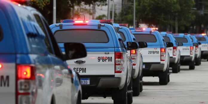 Row of blue and white police SUVs with red emergency lights flashing, parked in a line on a street view.